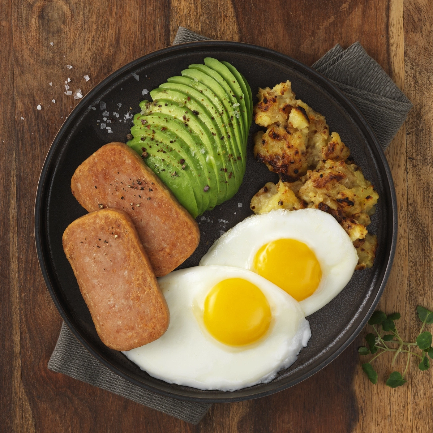 Ein Teller mit Spiegeleiern, geschnittenem Avocado, Bratkartoffeln und Spam.