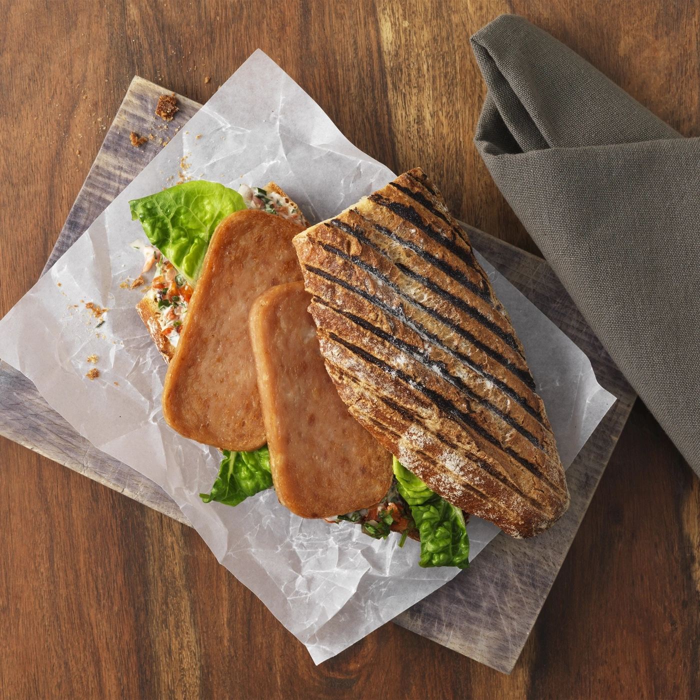 Ein gegrilltes Sandwich mit Fleisch und Salat auf einem Holzbrett.